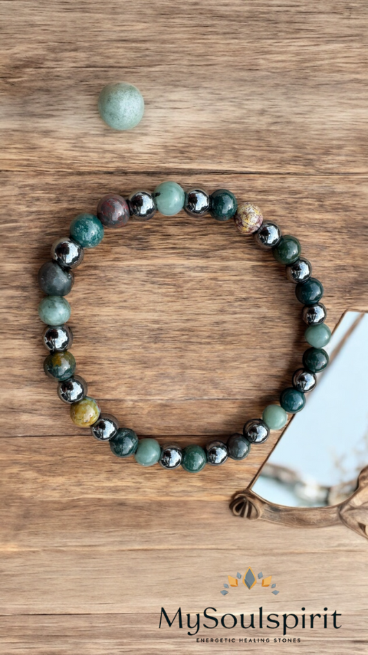 Heilsteinarmband aus grünen, silbernen und dunklen Perlen auf brauner Holzplatte