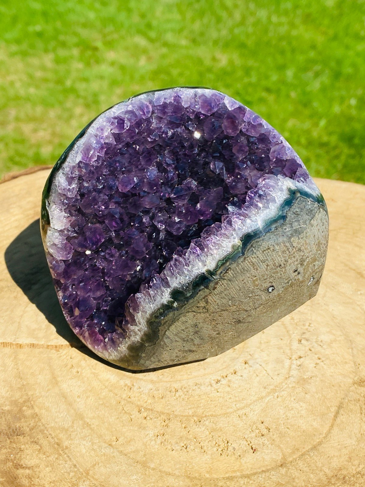 Halboffene Amethyst Druse auf Holzplatte vor grünem Rasen.